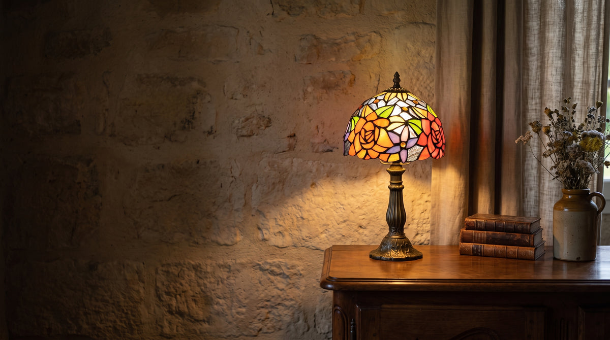 Lampe en vitrail à roses allumée sur une commode ancienne, mur en pierre d'une maison béarnaise